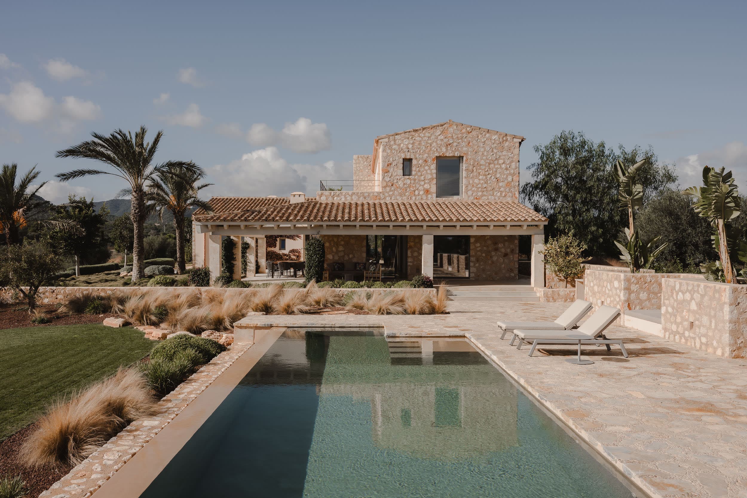 Finca de piedra con piscina, césped y palmeras en un jardín mediterráneo